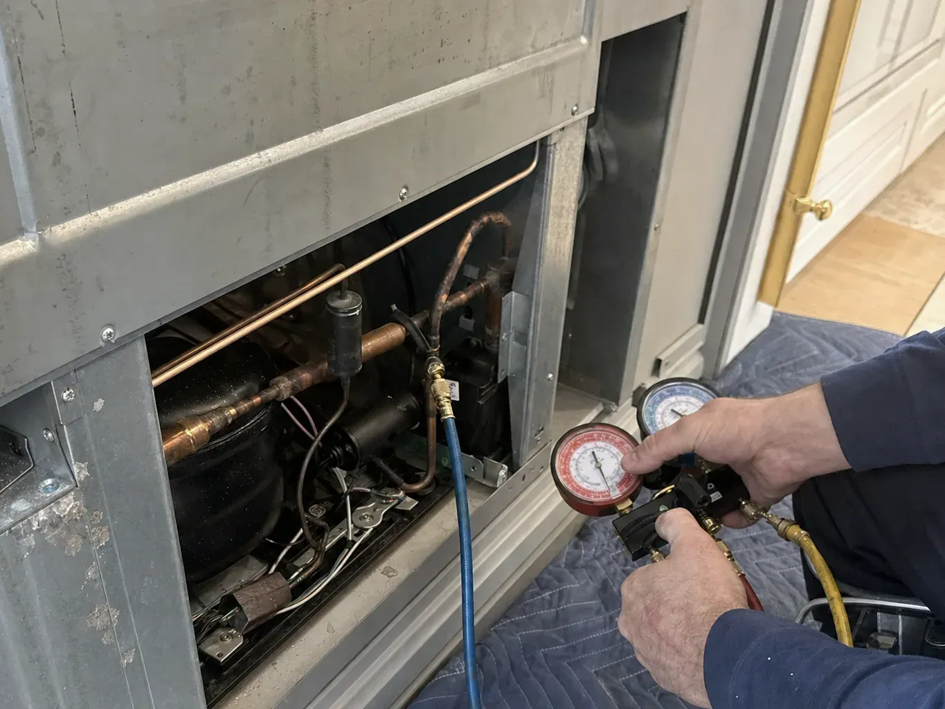 Hands holding refrigerant manifold gauges at an open compressor compartment
