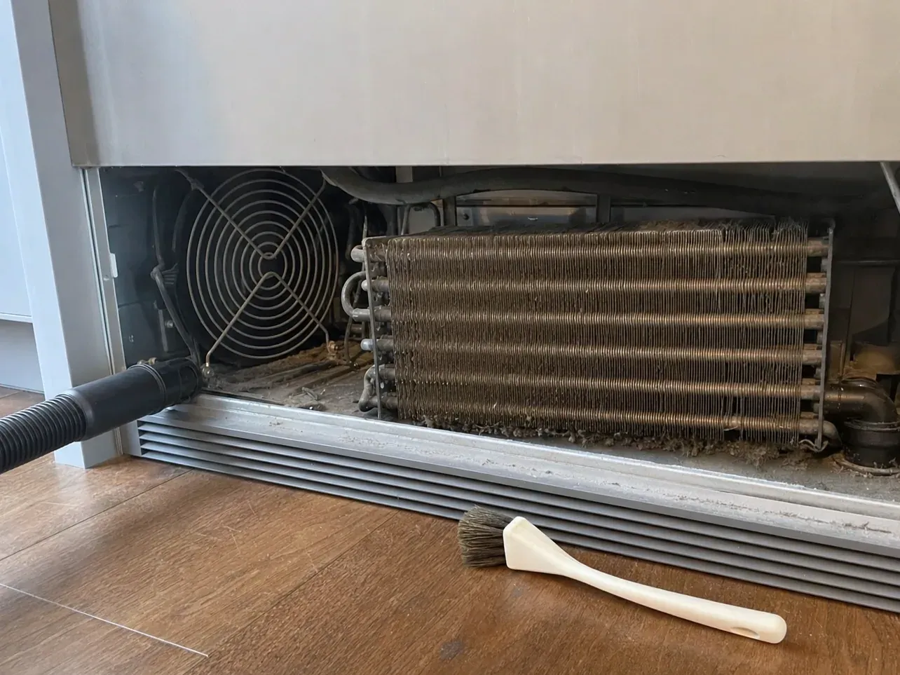 Condenser coil and fan under refrigerator with vacuum hose and brush
