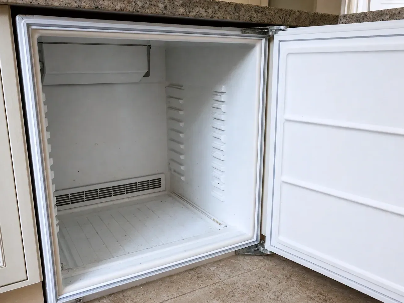 Empty white undercounter refrigerator compartment with door open in kitchen