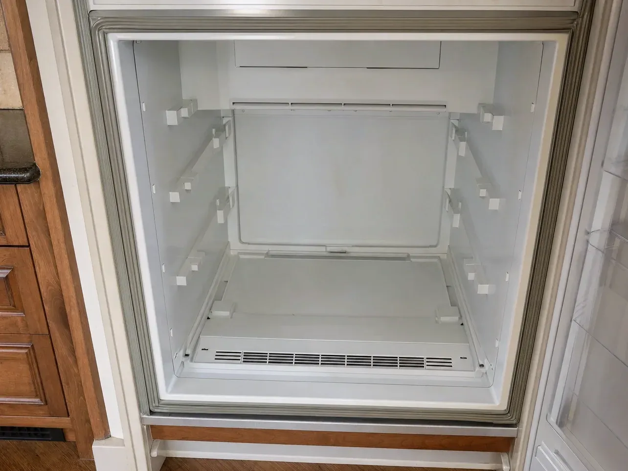 Empty freezer compartment with shelf brackets and floor vent grille visible