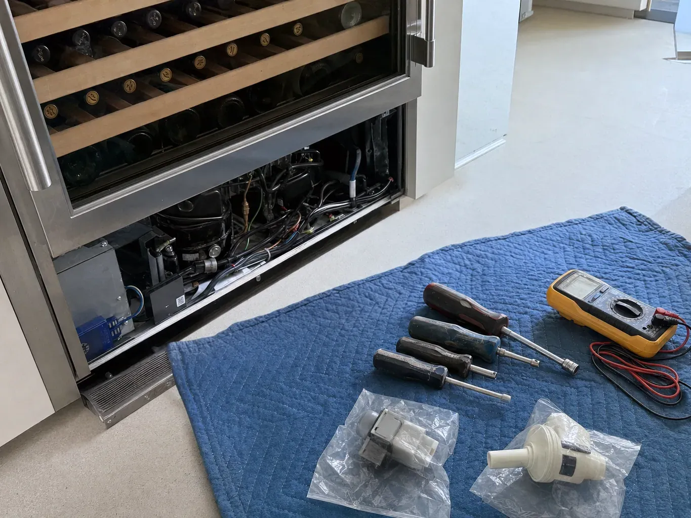 Wine cooler with lower grille off, screwdrivers, multimeter and parts on blanket