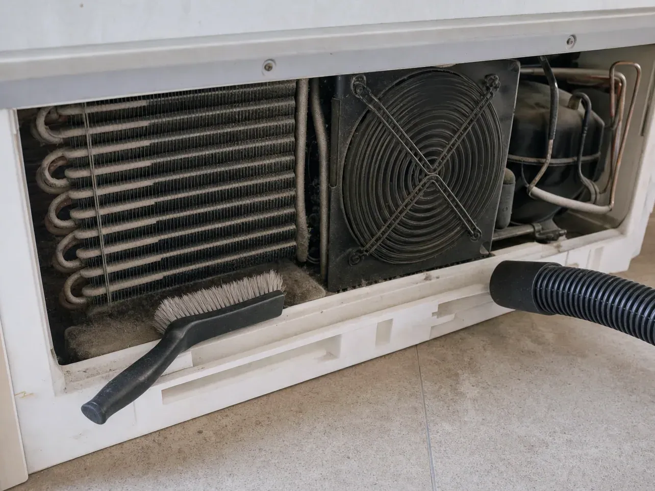 Dusty condenser coil and fan behind grille, brush and vacuum hose
