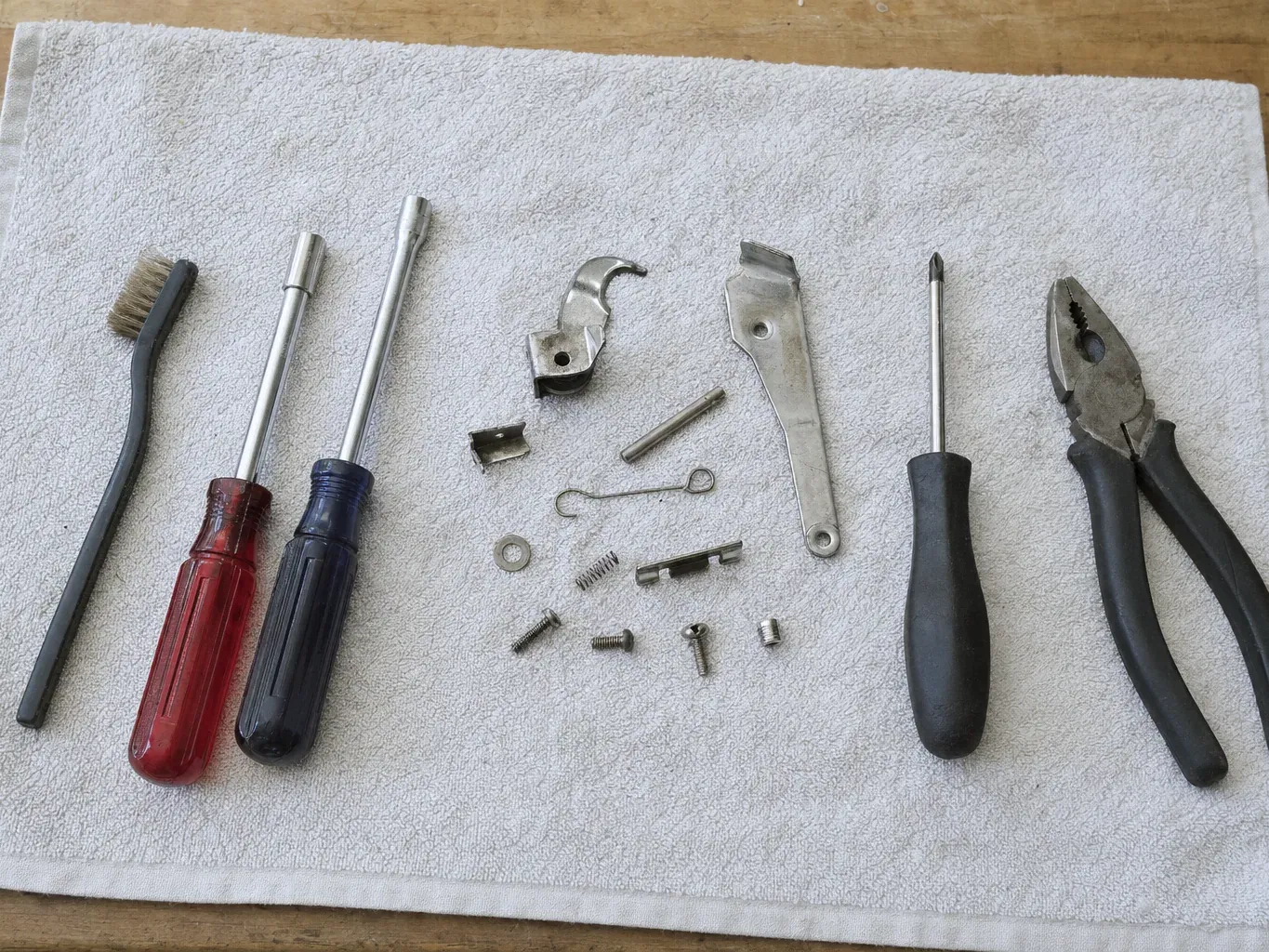 Pliers, screwdrivers, wire brush and latch parts on towel