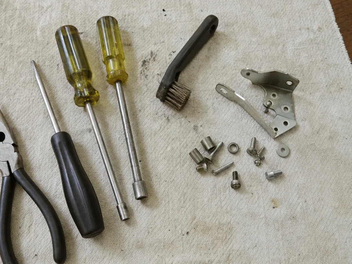 Bracket, screws, brush, two nut drivers and pliers on cloth