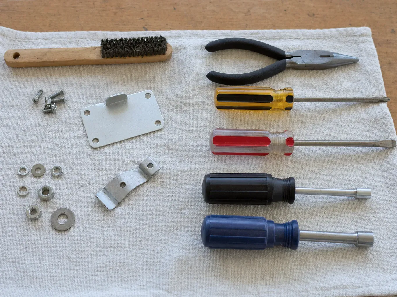 Screwdrivers, pliers, wire brush and small hardware laid on cloth