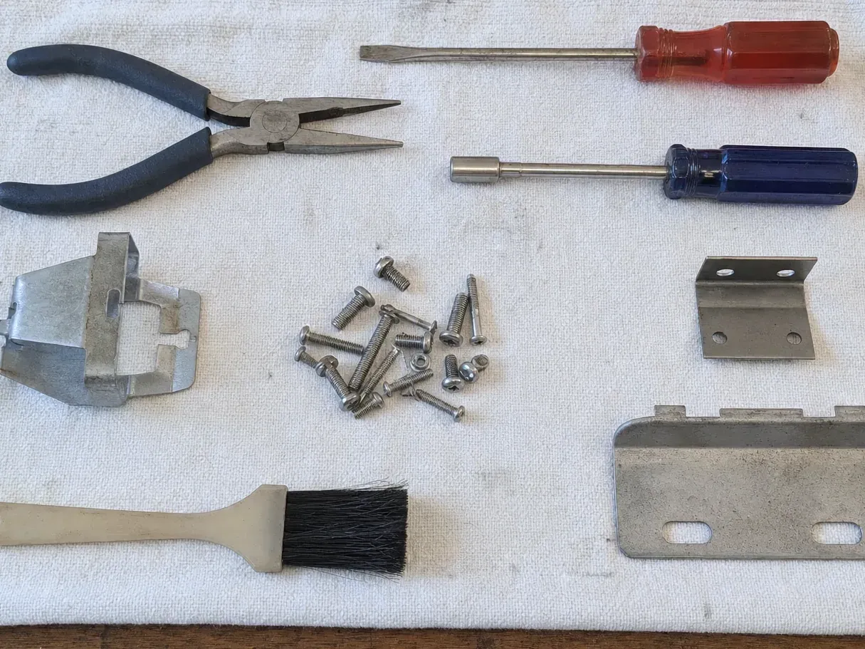 Screwdrivers, pliers, brackets, screws and a brush on white cloth