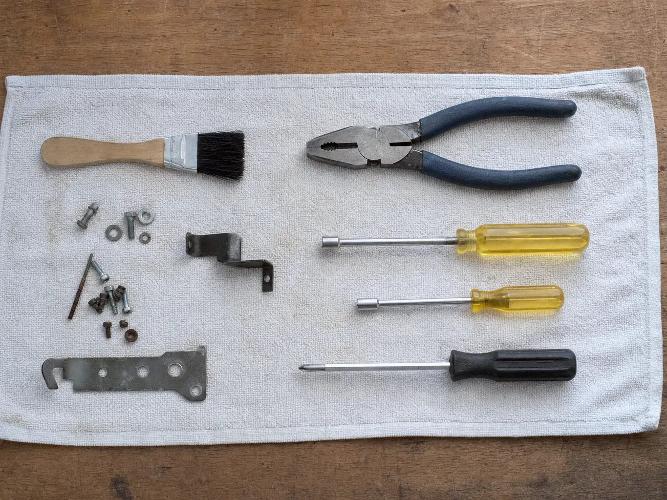 Pliers, brush, nut drivers and metal bracket on white towel