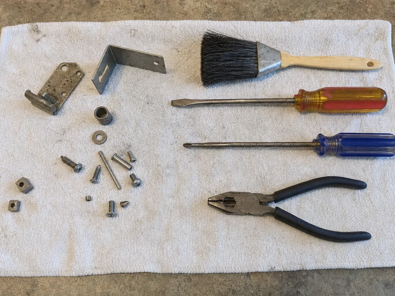 Paint brush, screwdrivers, pliers and hinge hardware on towel