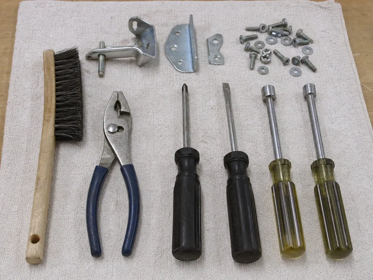 Screws, brackets, four screwdrivers, pliers and wire brush on towel