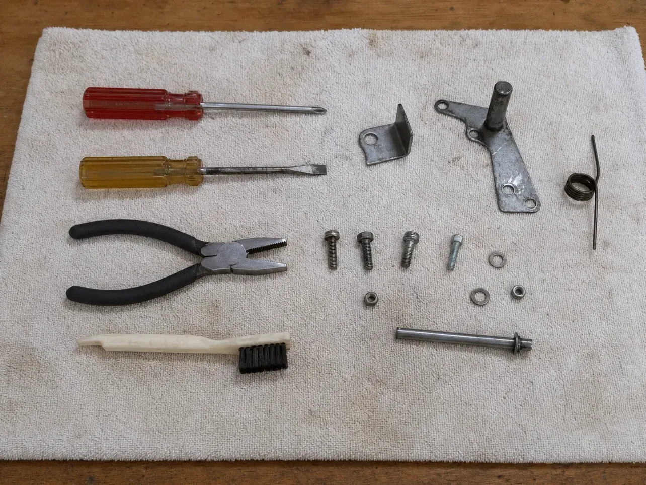 Spring, bracket, bolts, two screwdrivers, pliers and brush on towel