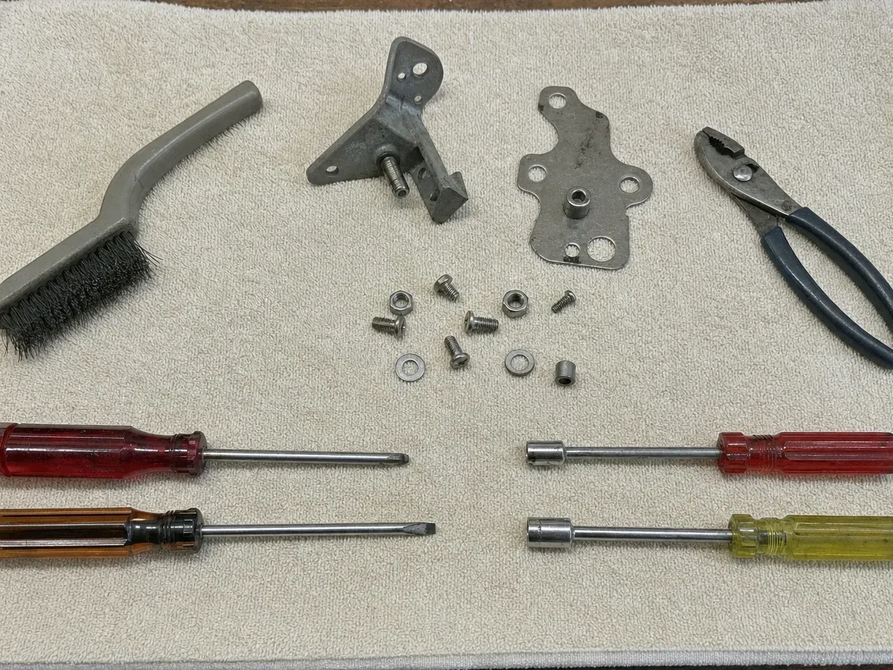 Pliers, hinge plates, screws, brush and four screwdrivers on a towel