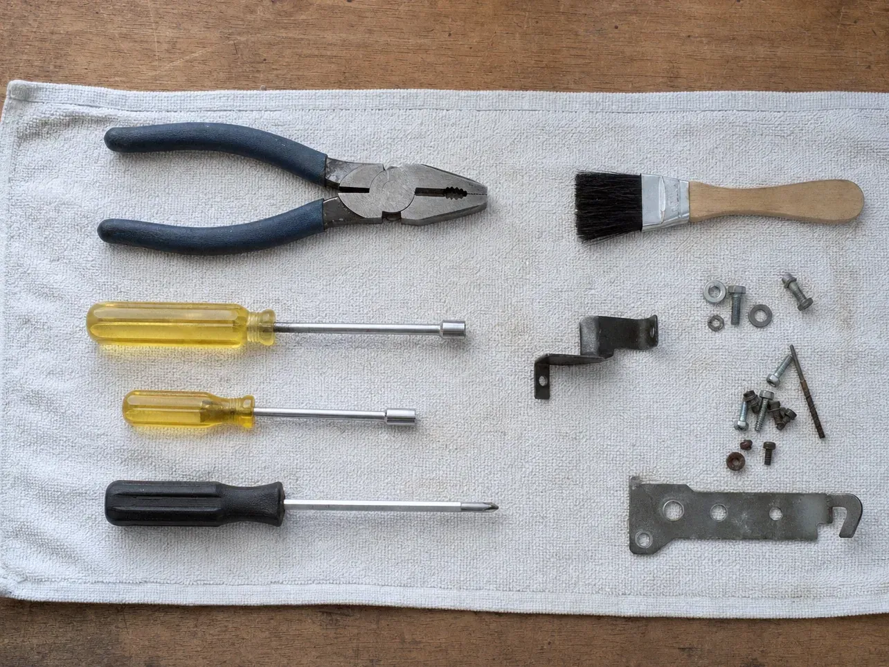 Paint brush, pliers, screwdrivers, bracket and screws on white towel