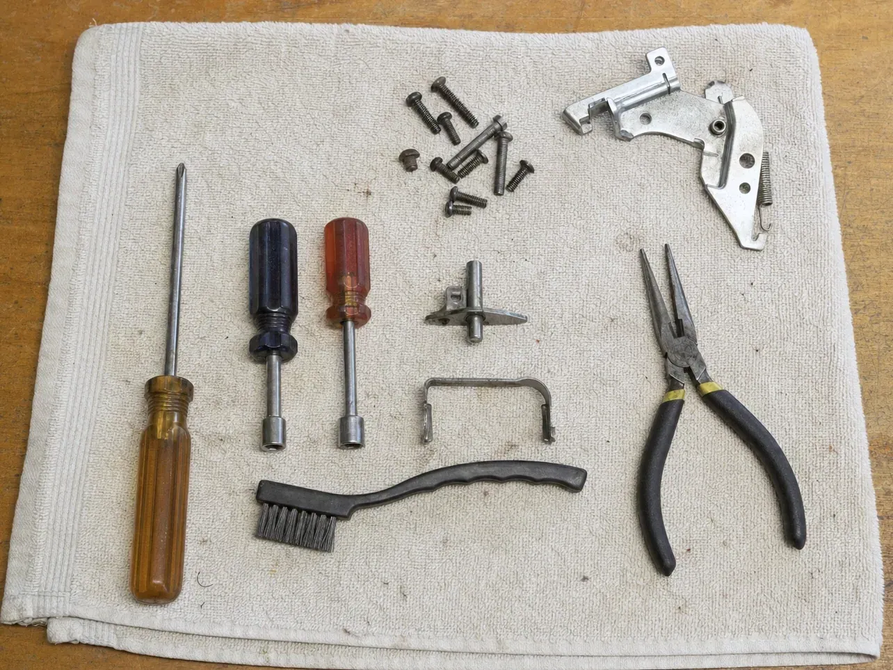 Needle-nose pliers, screwdrivers, hinge assembly and screws on a cloth