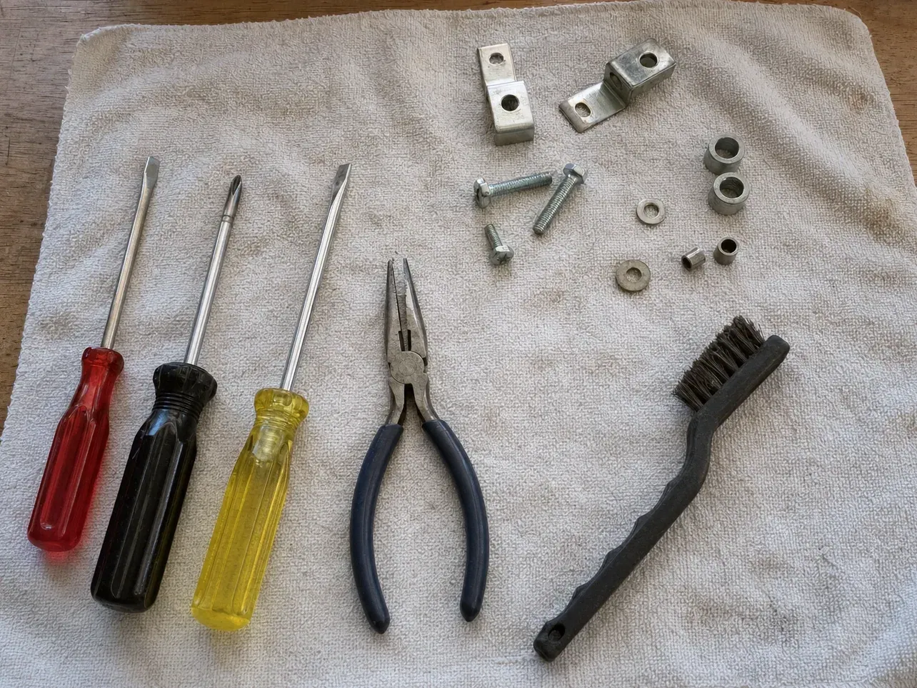 Brush, pliers and three screwdrivers with bolts on a towel