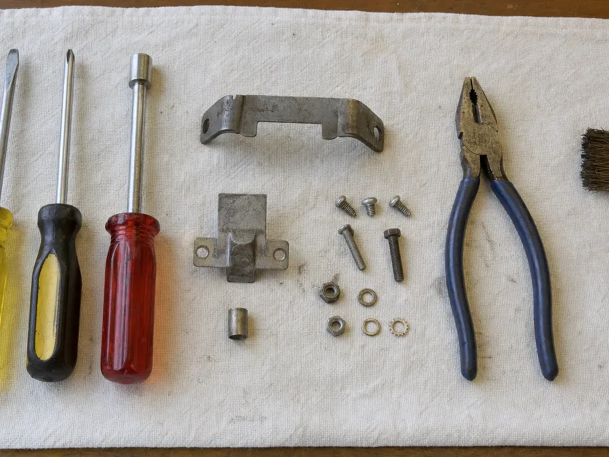 Pliers, brush, screwdrivers, bracket, screws and nuts on cloth