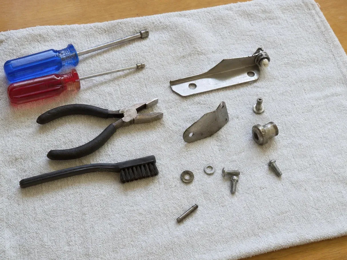 Metal brackets, screws, pliers and two nut drivers on cloth