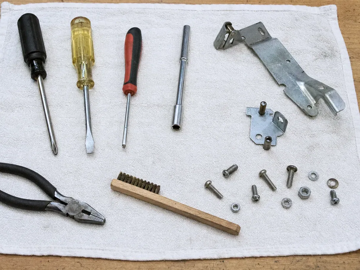 Metal hinge brackets, fasteners, screwdrivers and pliers on a towel